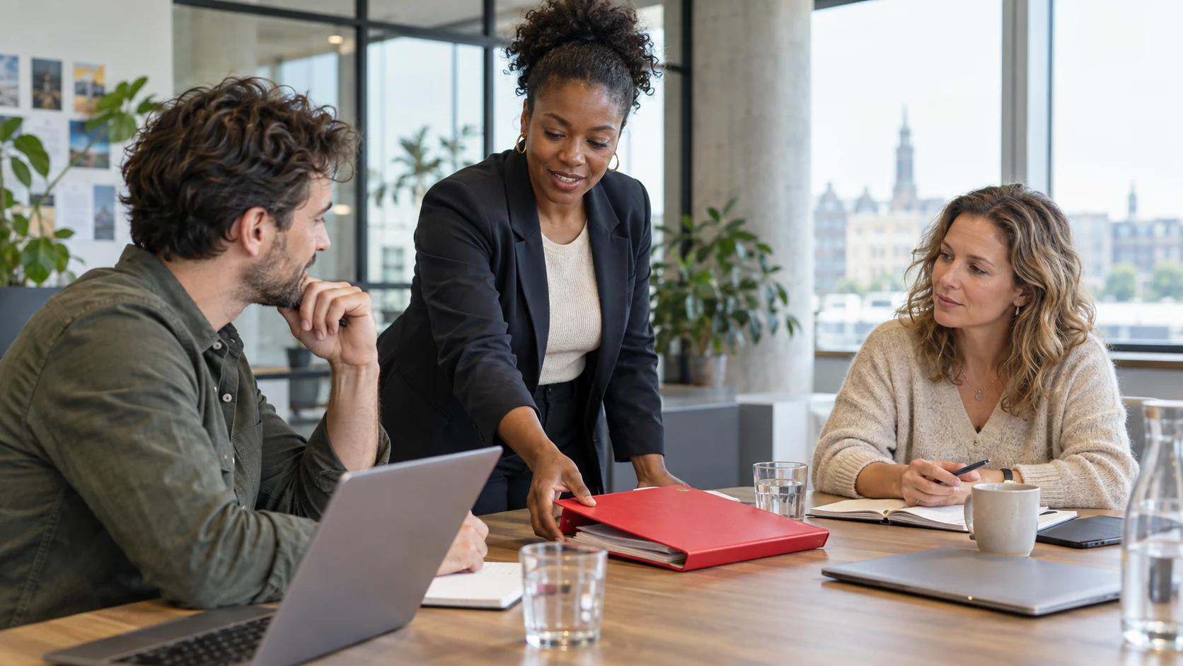 Drie ondernemers overleggen aan tafel met een rode documentenmap.